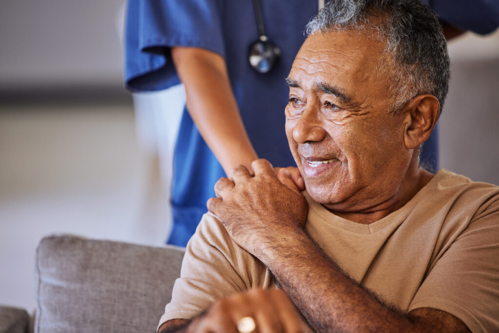 man smiling in hospital touching nurse's hand.