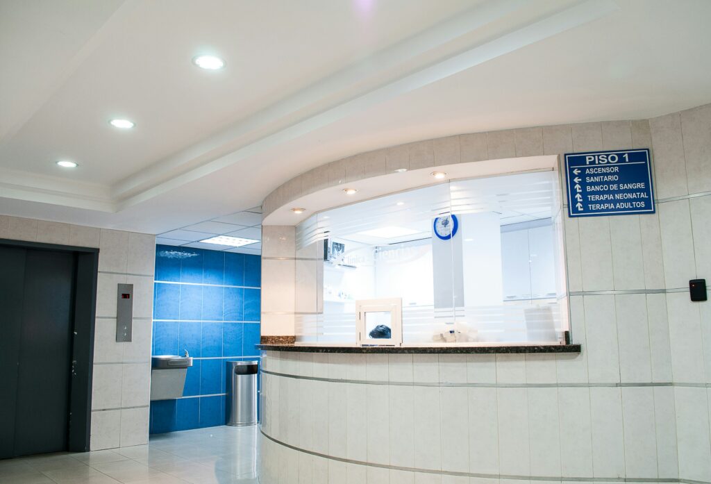 a hospital reception desk with doors to an elevator and water fountains behind it. The walls are white and blue