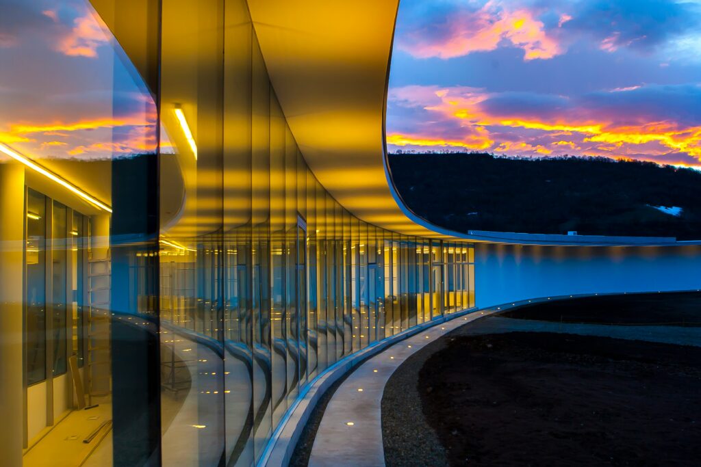 a curved glass wall lit by yellow lights underneath a cloudy sky