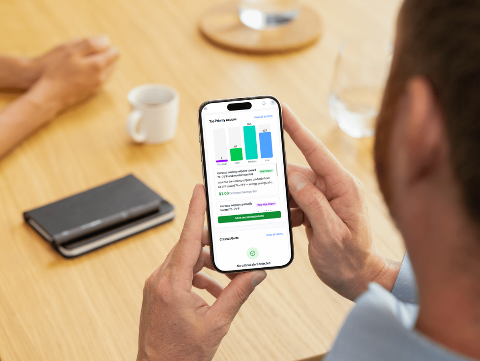 Man holding a smartphone using the Greenole platform, displaying priority action charts and alerts for smart building optimization.