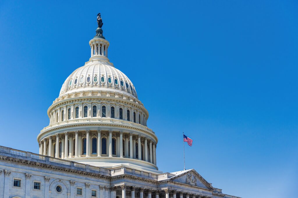 The white neoclassical dome of the United States Capitol Building with the American flag flying under a clear blue sky.